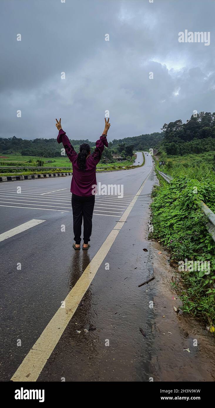 Mädchen isoliert, das an regnerischen Tagen in der Siegposition auf asphaltierten Straßen steht Stockfoto