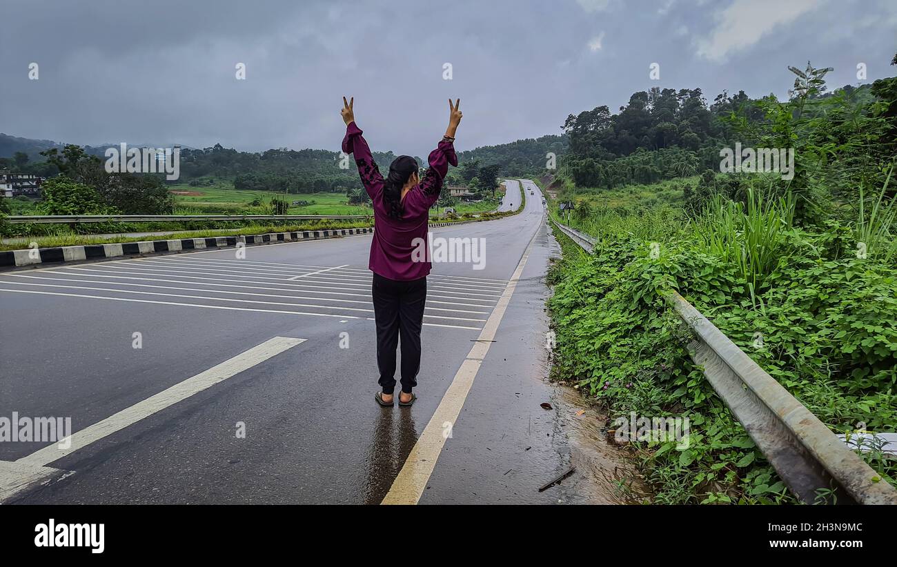 Mädchen isoliert, das an regnerischen Tagen in der Siegposition auf asphaltierten Straßen steht Stockfoto