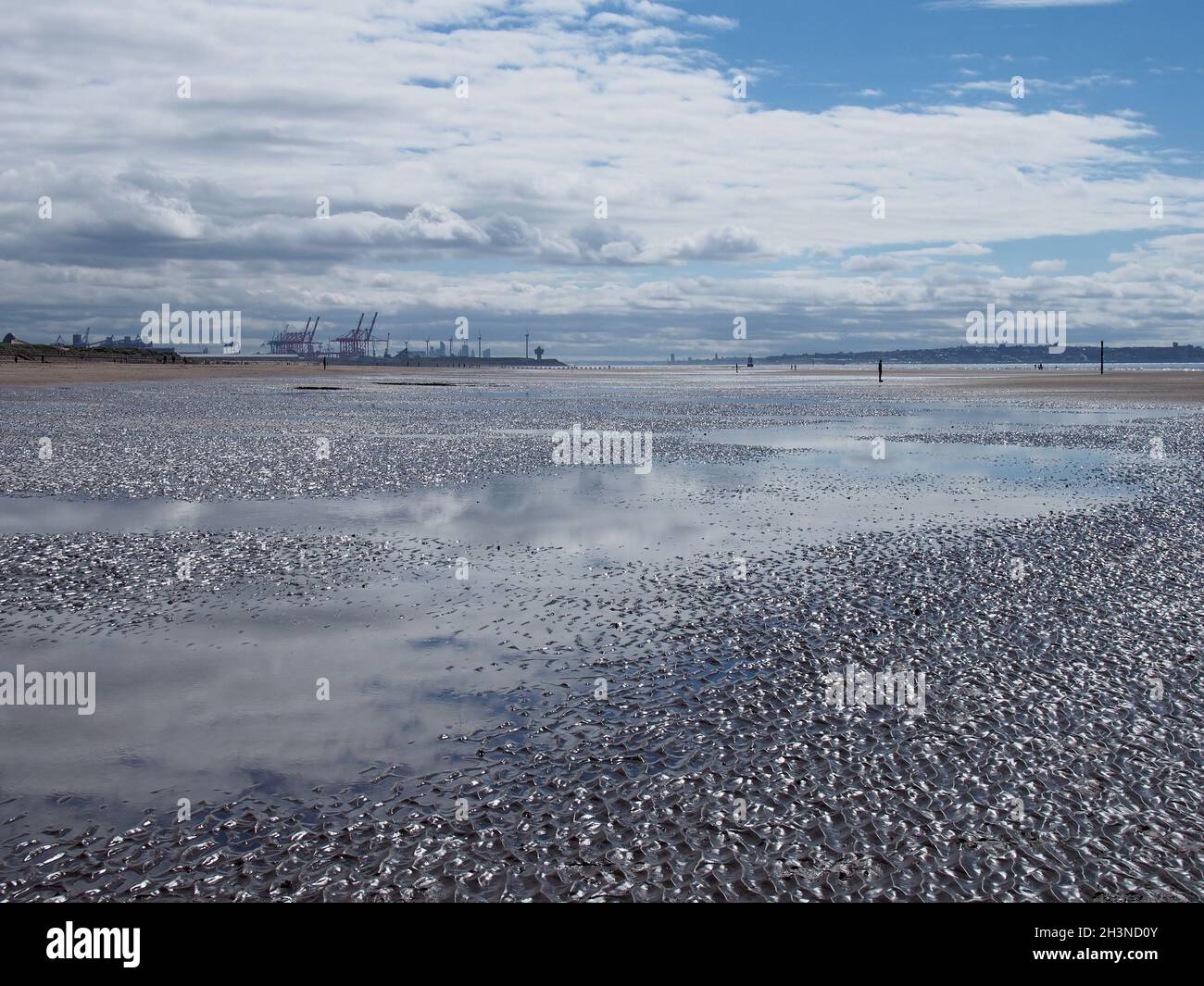 Der Strand von blundell Sands in der Nähe von southport mit Wasser von der ankommenden Flut spiegelt den Himmel und liverpool Stadt und Container Stockfoto