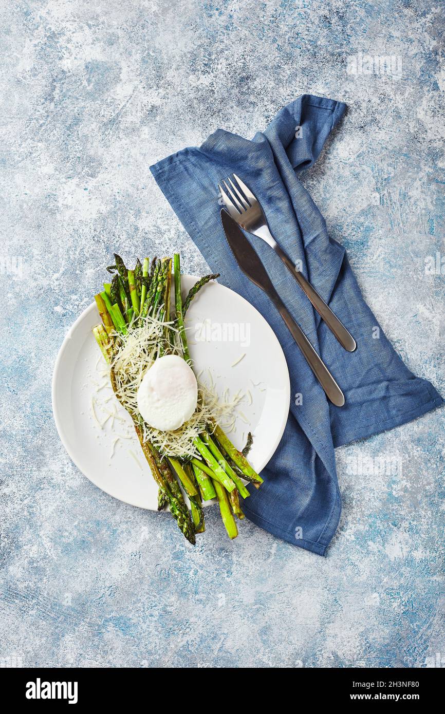 Grüner Spargel mit pochiertem Ei und Parmesan, vegetarisches Frühstück auf weißem Teller auf hellem Hintergrund. Stockfoto