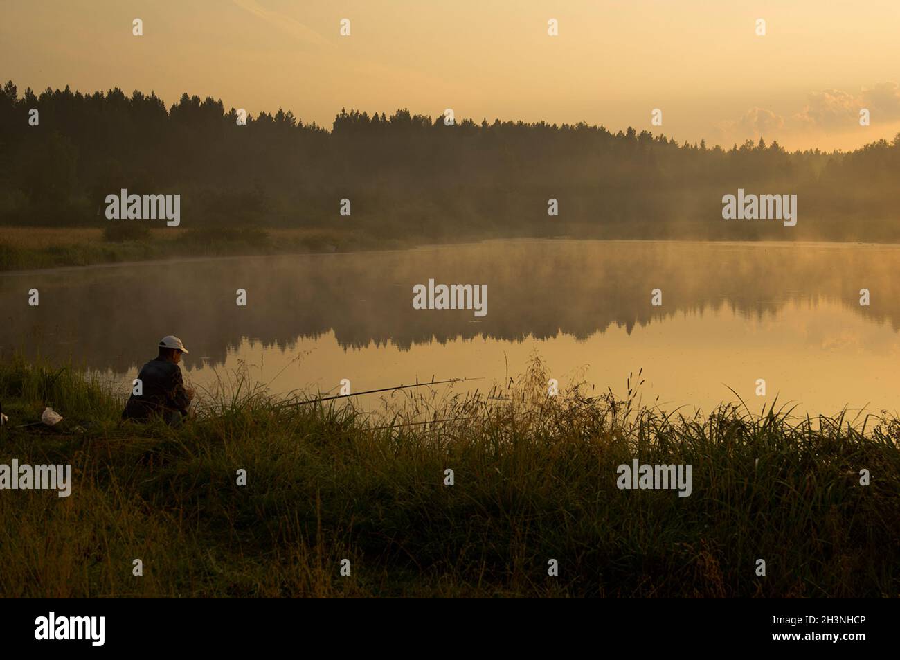 Ein Fischer bei Sonnenuntergang am Teich fängt Fische. Stockfoto