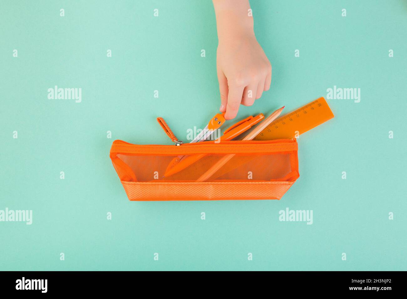 Kinderhand, die alle Stifte, Stifte, Scheren usw. in einem orangefarbenen Etui hält. Zurück zum Schulkonzept Stockfoto