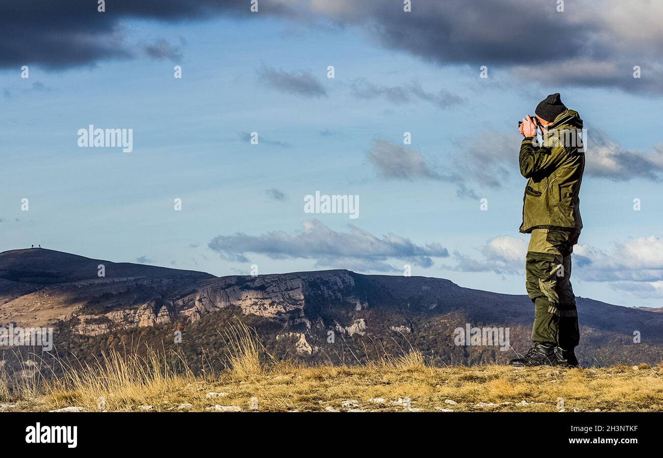 Der Mensch steht auf dem Berg und fotografiert die Landschaft der Berge und des Herbstwaldes. Stockfoto