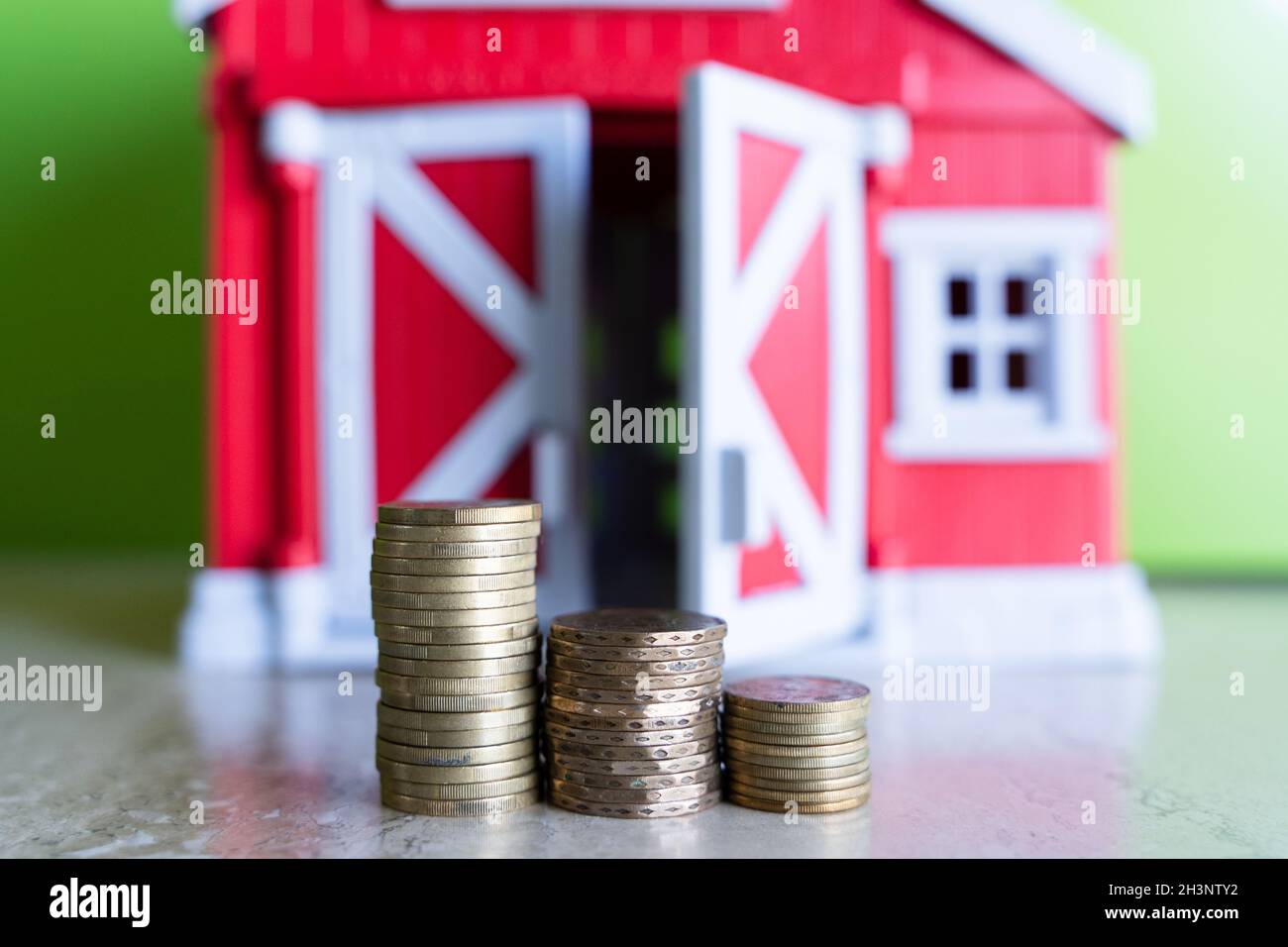 Münzleiter mit rotem Spielzeughaus im Hintergrund. Hausversicherung, Investitionen, Immobilienmarkt Konzept Stockfoto