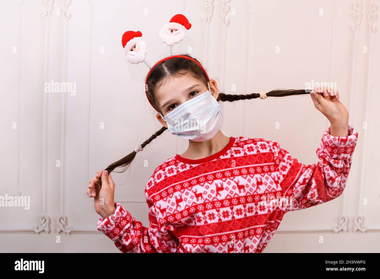 Kind in einer schützenden medizinischen Maske im neuen Jahr. Ein Teenager-Mädchen hält ihre Zöpfe. Stockfoto