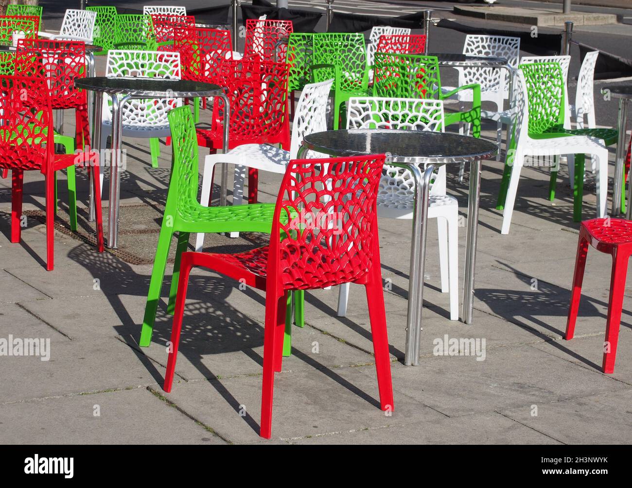 Farbenfrohe, im italienischen Stil gehaltene Café-Stühle und -Tische im Freien auf der Straße, die bei Sonnenlicht im Sommer in rot-grünen und weißen Farben gehalten werden Stockfoto
