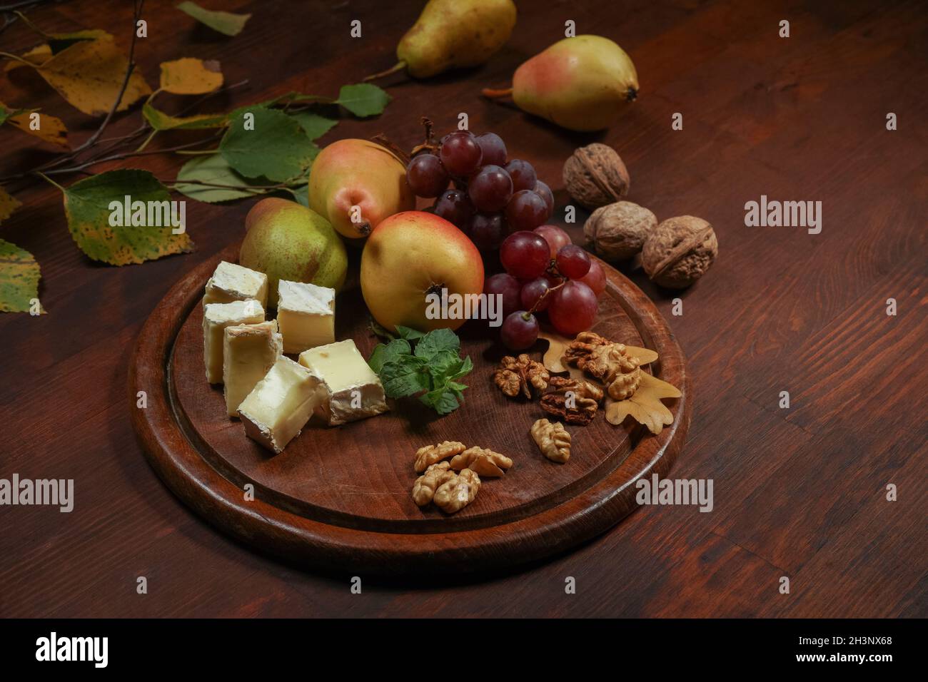 Bestes Wein-Snack-Set: Käse, Trauben, Birne und drei Walnüsse auf einem Holztisch. Brie-Käse mit Früchten, Trauben, Walnüssen auf einem da Stockfoto