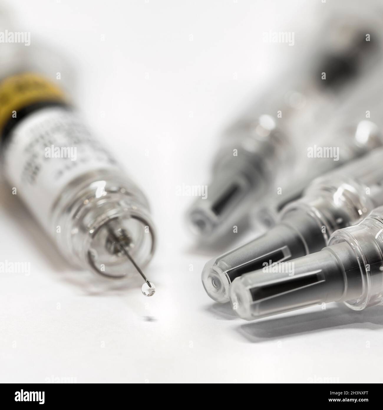 Spritze mit Impfstoff gegen Coronavirus auf einem Tisch. Ein Tropfen hängt von der Spitze der Nadel. Stockfoto