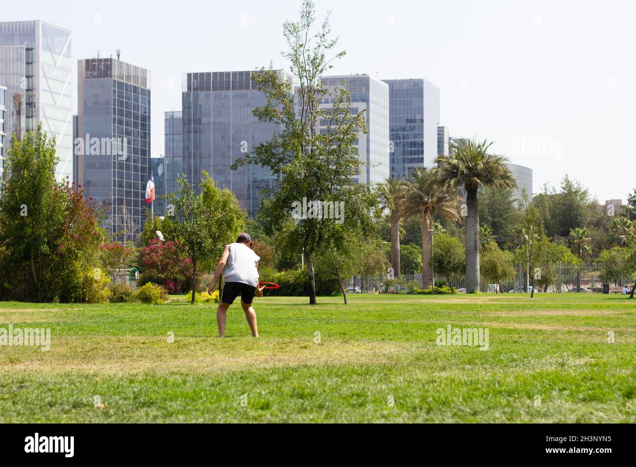 Junger Mann, der am sonnigen Tag im Park mit Frisbee spielt, und Finanzgebäude im Hintergrund. Arbeits- und Freizeitkonzepte Stockfoto