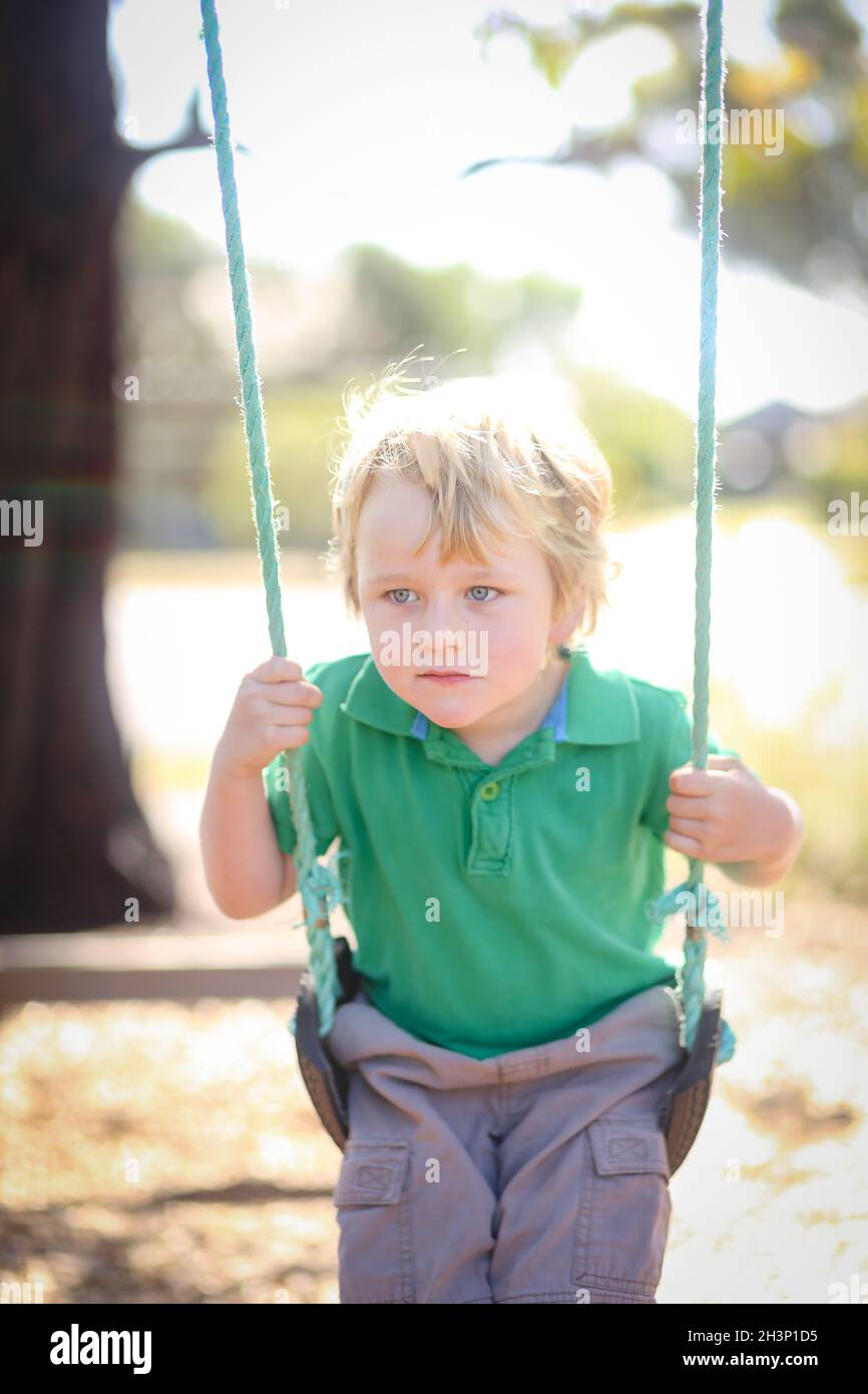 Kleiner blonder Junge, der in kindligen Porträts auf Schaukel im Kindergarten spielt Stockfoto