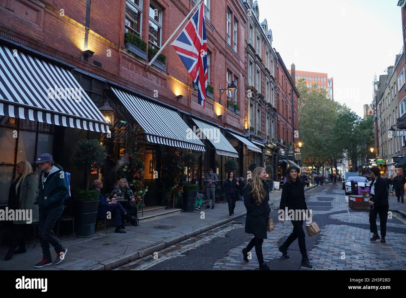 London, Großbritannien, 29. Oktober 2021: Während die Abenddämmerung in Covent Garden und den umliegenden gepflasterten Straßen einbricht, genießen Touristen und Einkäufer einen trockenen Zauber zwischen Regenschauern. Diners und Trinker in Bars, Pubs oder Restaurants haben oft die Wahl, drinnen oder draußen zu sitzen. Werbekampagnen, die Menschen zu einem Besuch in London ermutigen, scheinen viele halbzeitige Familienbesuche angelockt zu haben, und London hat derzeit eine geringere Rate an kovidierten Infektionen als einige andere Gebiete des Landes. Im zentralen Marktbereich sind bereits Weihnachtsdekorationen zu sehen. Anna Watson/Alamy Live News Stockfoto