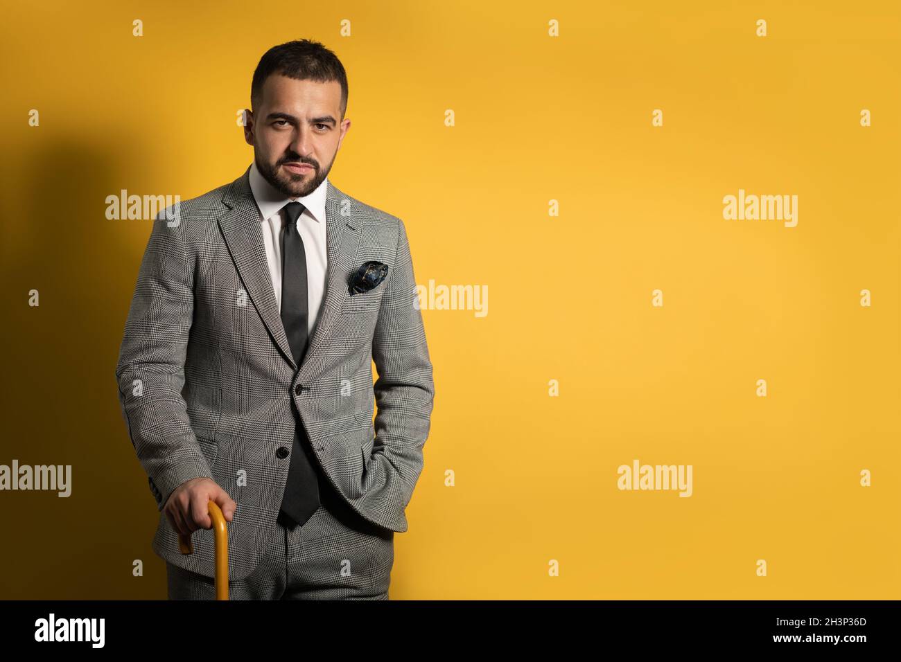 Old School trendy stylish hübscher junger Mann in grauem Anzug mit einer Hand angehoben stehend mit Stock oder Regenschirm in der Hand i Stockfoto