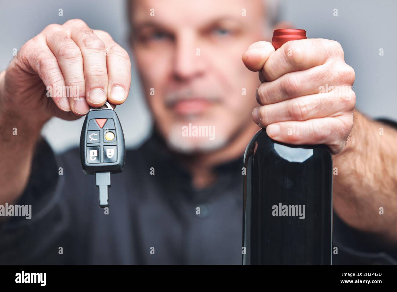 Ein älterer Mann, der eine unbeschriftete Flasche Rotwein und Autoschlüssel an die Kamera hält, in einem Konzept des Trinkens und Fahrens mit Fokus auf seine Hände Stockfoto
