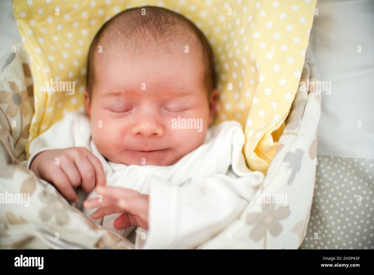 Niedliches neugeborenes Baby, das im Wickel mit Lächeln auf dem Bett schläft Ihr Gesicht Stockfoto