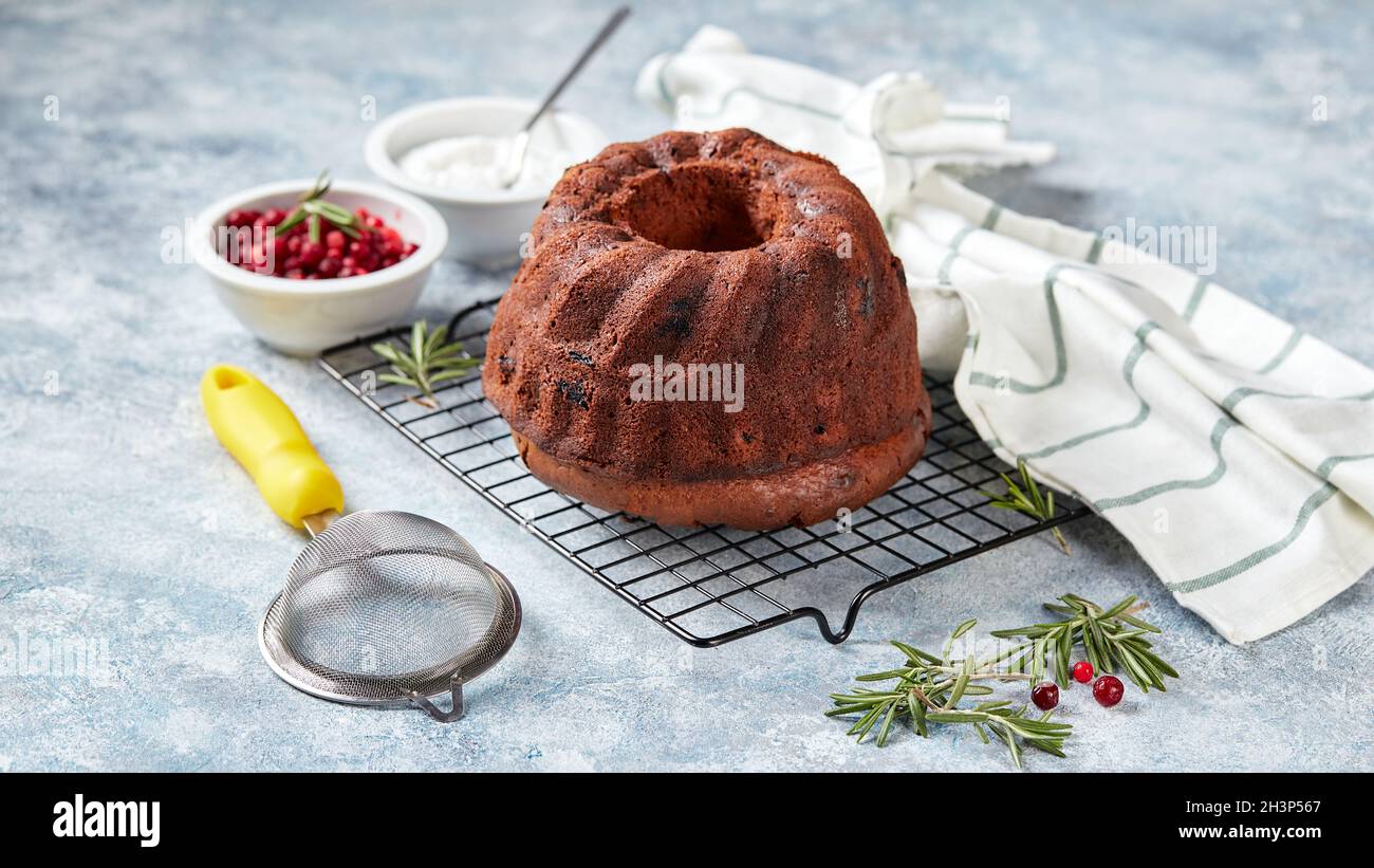 Schokoladenkuchen auf einem Metalldrahtgestell, Puderzucker und Preiselbeeren in Schüsseln Stockfoto