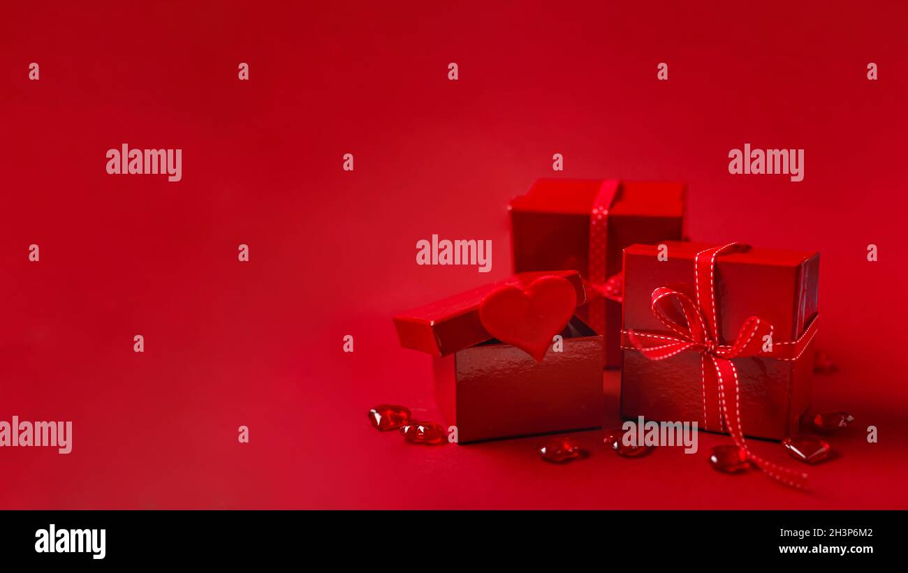 Rote Geschenkschachteln mit rotem Band und dekorativen Herzen auf rotem Hintergrund Stockfoto