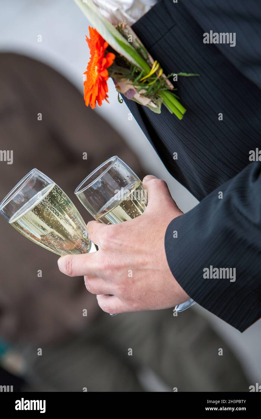 Der Bräutigam hält ein Glas oder eine Flöte Champagner auf dem Hintergrund der Freunde über die Natur bei der Hochzeitszeremonie. Nahaufnahme. Toas Stockfoto