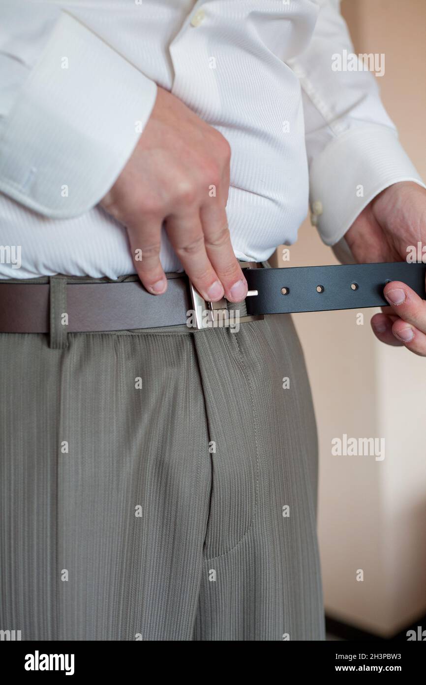 Ein Mann in Hose und Hemd knöpfte einen schwarzen Ledergürtel. Bräutigam Dress up ein Gürtel mit Schnalle. Geschäftsmann tragen Lederstil Stockfoto