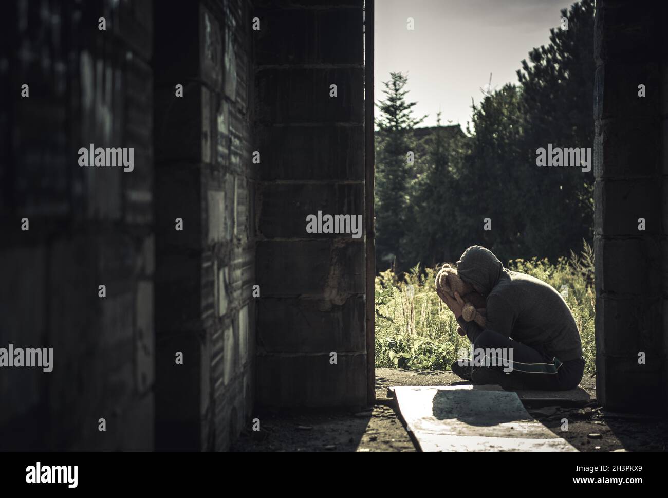 Männer mit geistiger Störung umarmen sein Teddybär-Spielzeug vor den Hausruinen. Thema des Konzepts „Obdachlosigkeit und psychische Krankheit“. Stockfoto