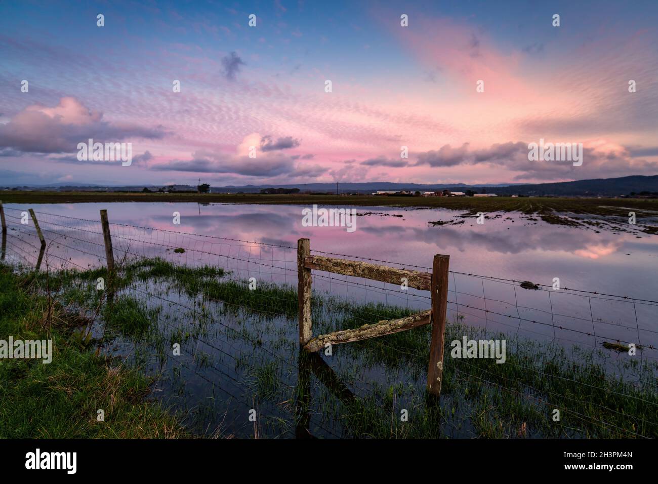 Farbbild eines Zauns in einem überfluteten Feld bei Sonnenuntergang. Stockfoto