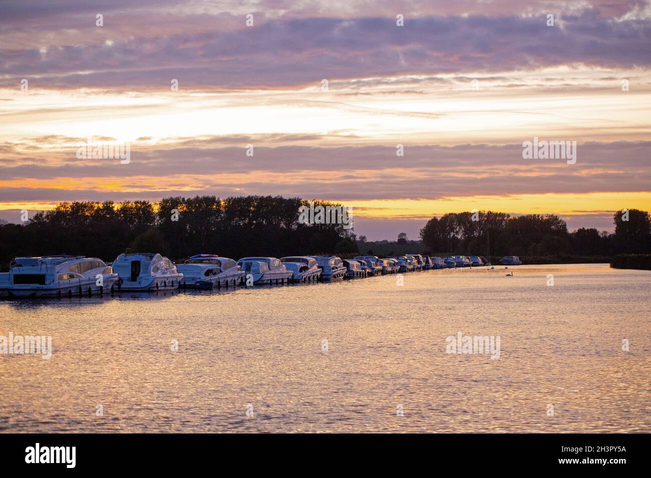 Abenduntergang. Bunte Wolkenschichten spiegeln sich auf der Oberfläche des River Bure, mit Liegeplätzen bespiegelten Booten. Acle Bridge, Broadland, Norfolk, Nationalpark. Urlaub, Stockfoto