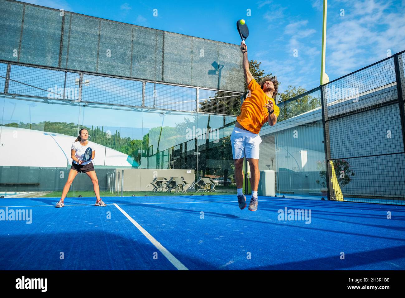 Gemischtes Padel-Match auf einem Padel-Platz mit blauem Gras - wunderschönes Mädchen und hübscher Mann, der im Freien Padel spielt Stockfoto