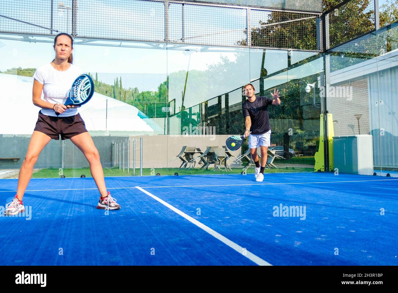 Gemischtes Padel-Match auf einem Padel-Platz mit blauem Gras - wunderschönes Mädchen und hübscher Mann, der im Freien Padel spielt Stockfoto