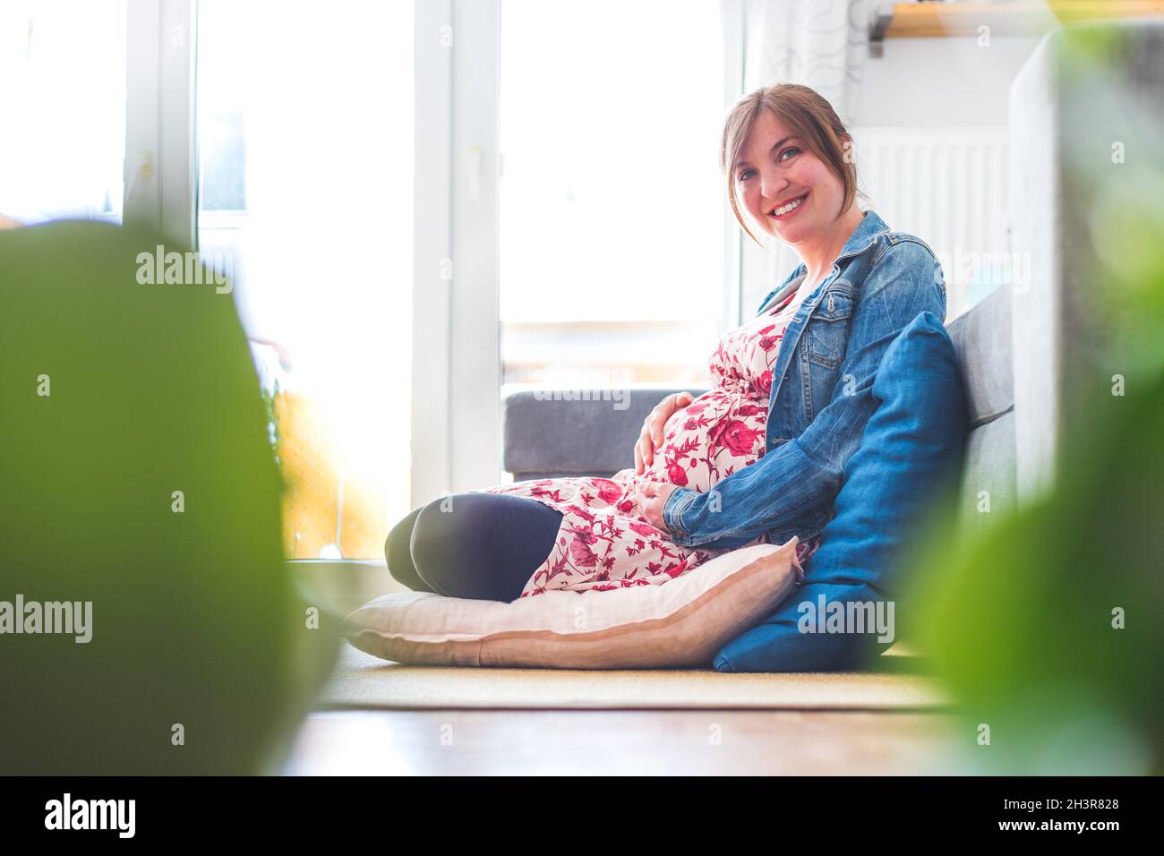 Eine glückliche, schwanger Mutter sitzt auf dem Boden und umarmt ihren Bauch Stockfoto