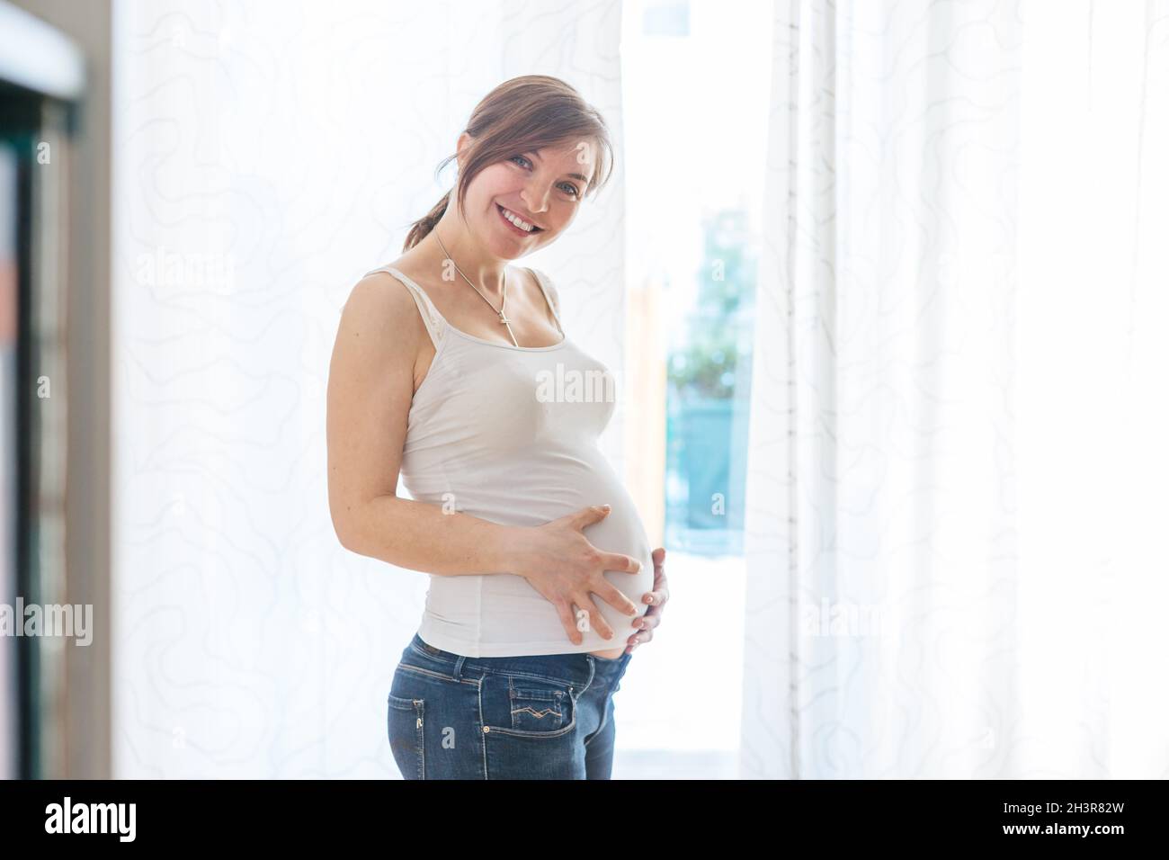 Glückliche, schwanger Mutter in blauen Jeans umarmt ihren nackten Bauch, aus nächster Nähe Stockfoto