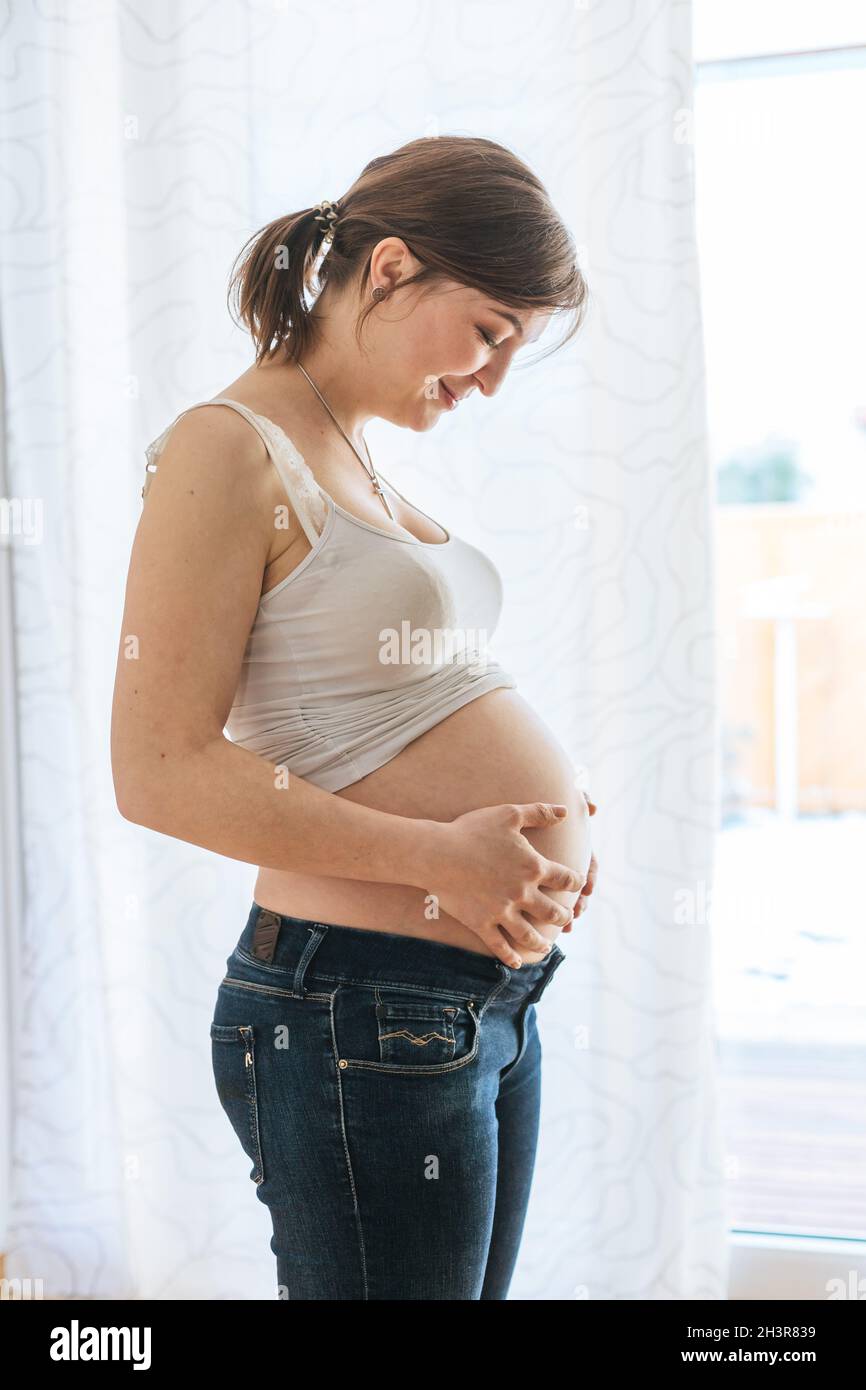 Glückliche, schwanger Mutter in blauen Jeans umarmt ihren Bauch, aus nächster Nähe Stockfoto