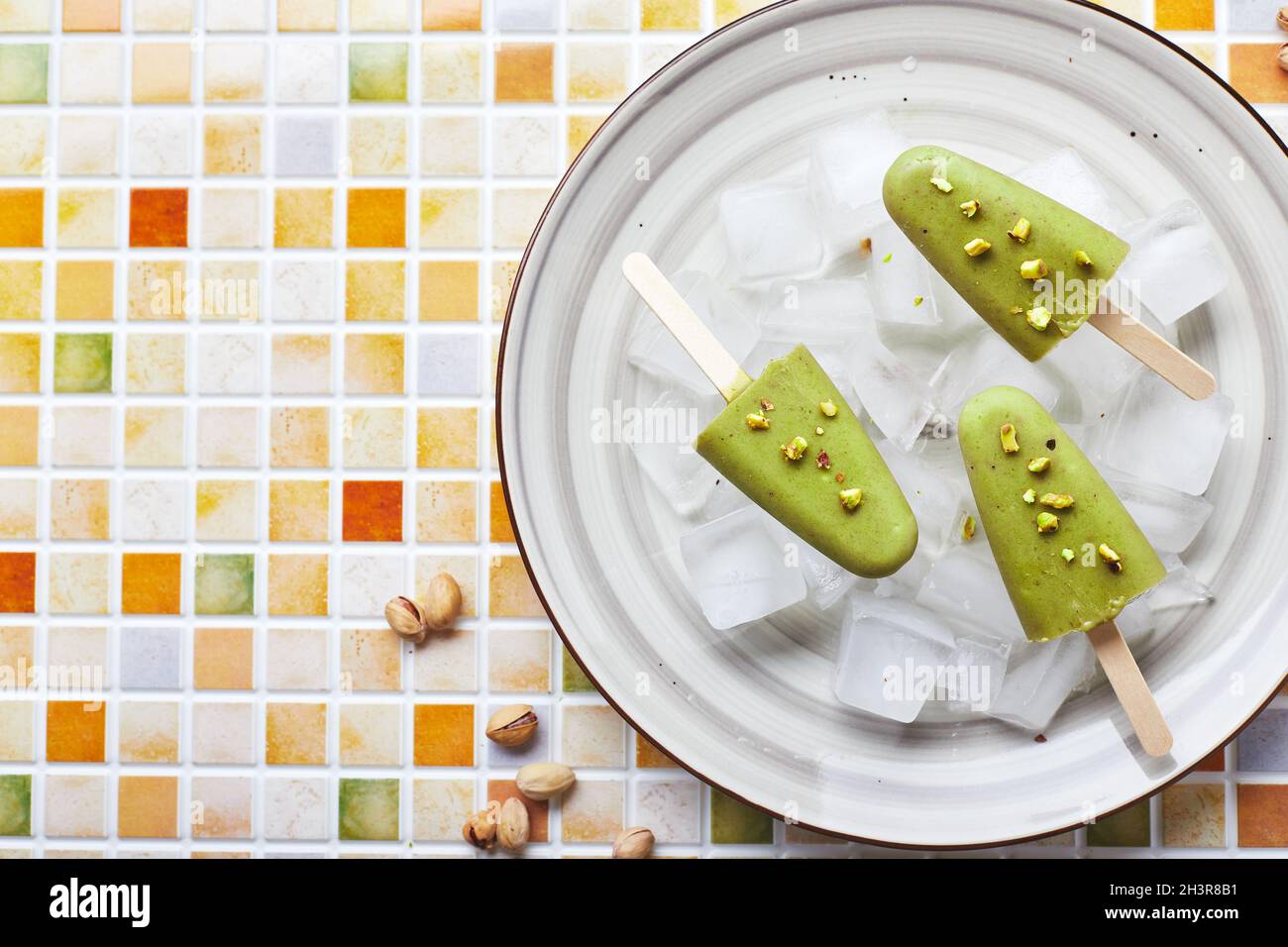 Gefrorener hausgemachter Pistazien-Popsicle in einer Schüssel mit Eis auf einem Tisch mit Mosaikfliesen. Erfrischender Fruchteis, gefrorener grüner Saft auf Stick. Oben vi Stockfoto