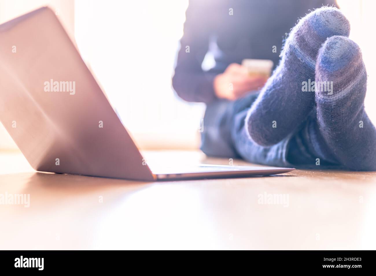 Junger Mann mit warmen Socken und Laptop im Vordergrund auf dem Holzboden, hell Stockfoto