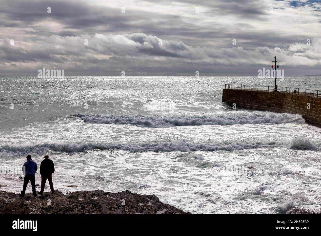 PORTHLEVEN, CORNWALL, UK - MAI 11 : stürmisches Wetter an der Hafenmauer in Porthleven, Cornwall am 11. Mai 2021. Zwei nicht identifizierte Stockfoto