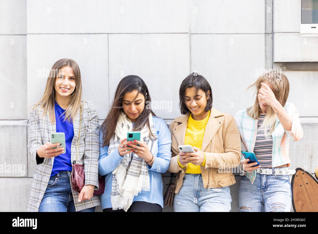 Multiethnische Gruppe von schönen jungen Freundinnen, die mit mobilen Smartphones an einer Wand stehen Stockfoto