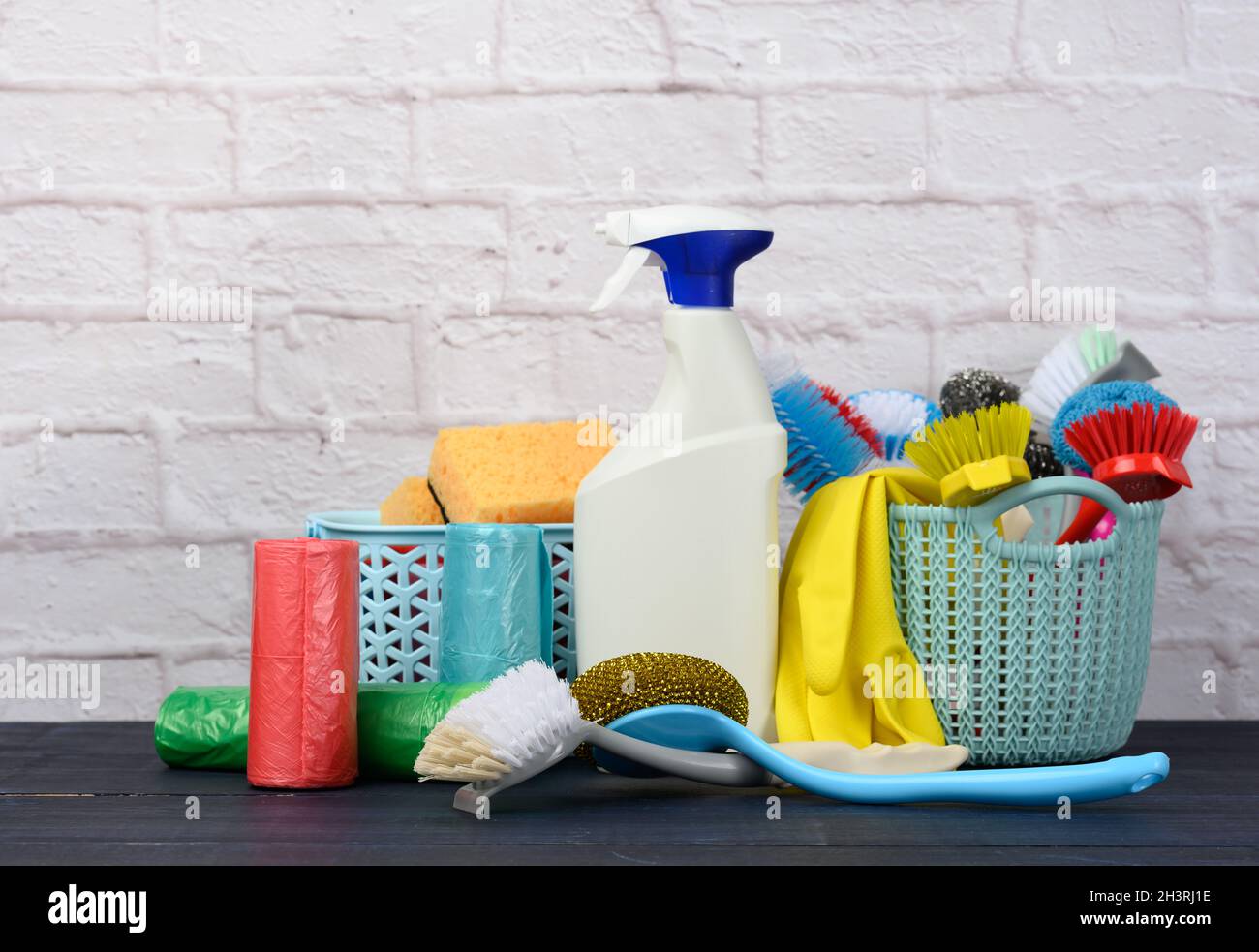 Schwämme, Plastikbürsten und Waschmittelflaschen auf einem blauen Holztisch. Haushaltsreinigungsgegenstände auf weißem Backgrou aus Ziegelsteinen Stockfoto