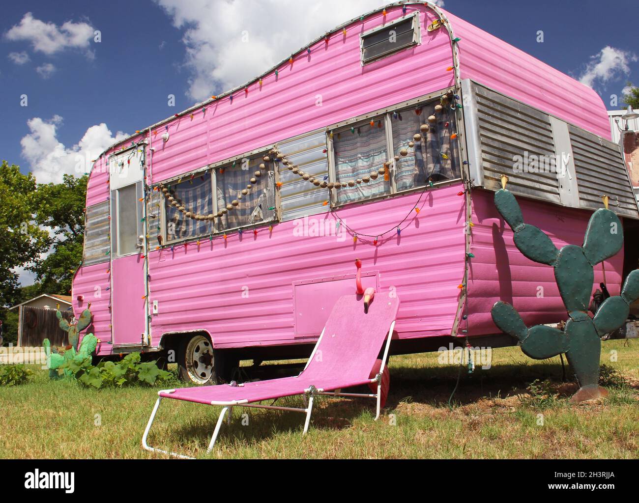 Pinker Reisetrailer mit Stuhl und Kaktus plus blauem Himmel und Wolken Stockfoto