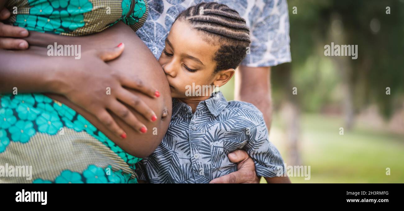 Glückliche afrikanische Familie erwartet anderes Baby - Nahaufnahme Kind küsst Bauch seiner Schwangeren Mutter - Eltern lieben und Mutterschaft Lifestyle-Konzept Stockfoto