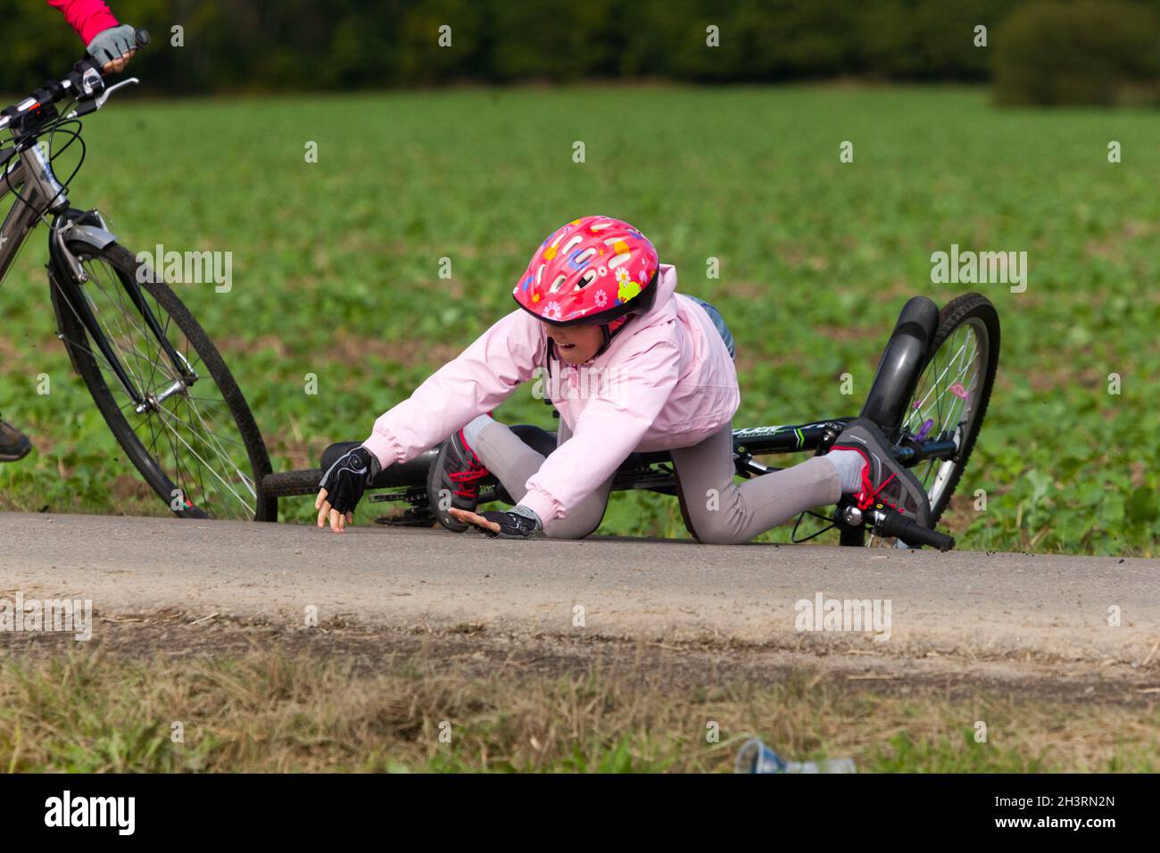 Kind fällt vom Fahrrad, Straßenunfall, ein Mädchen mit Fahrradhelm Stockfoto