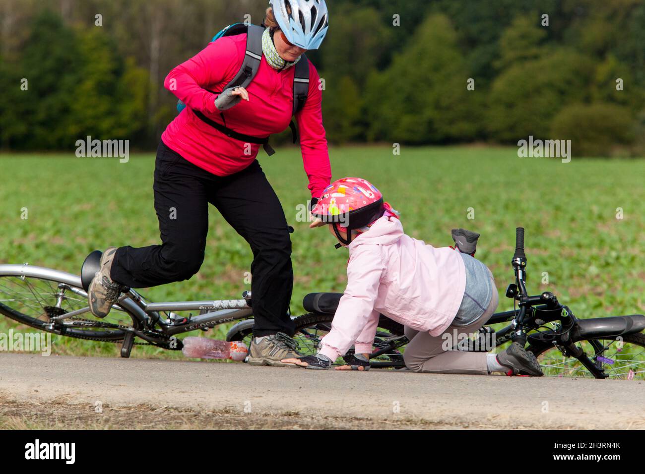Kind nach dem Sturz vom Fahrrad, ein Mädchen mit einem Fahrradhelm, eine Frau eilt um Hilfe Stockfoto