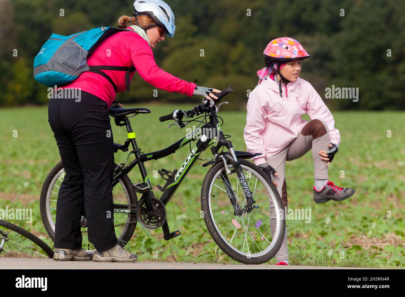 Kind nach dem Sturz vom Fahrrad streichelt ein Mädchen mit einem Fahrradhelm ihr angestoßenes Knie Stockfoto
