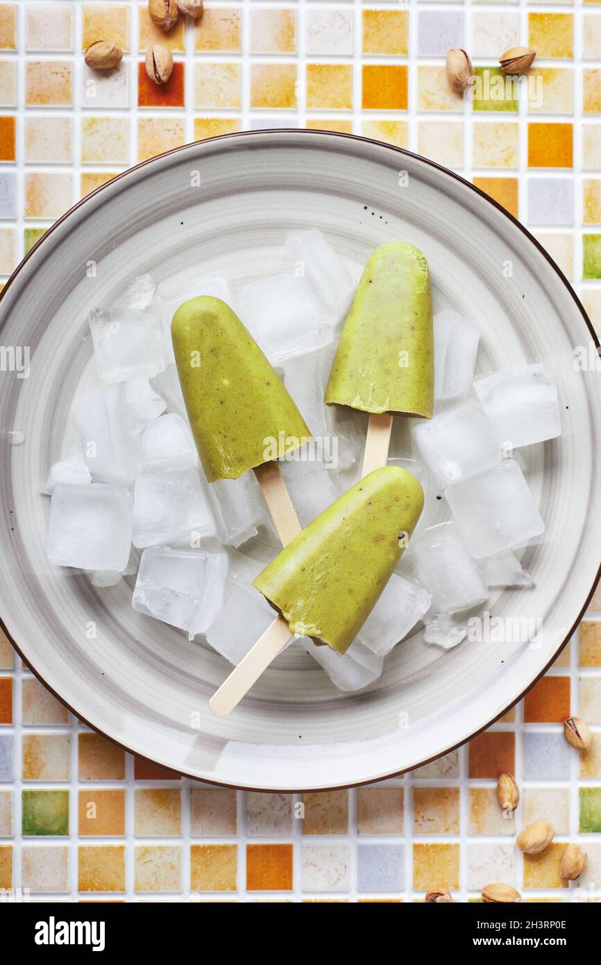 Gefrorener hausgemachter Pistazien-Popsicle in einer Schüssel mit Eis auf einem Tisch mit Mosaikfliesen. Erfrischender Fruchteis, gefrorener grüner Saft auf Stick. Oben vi Stockfoto