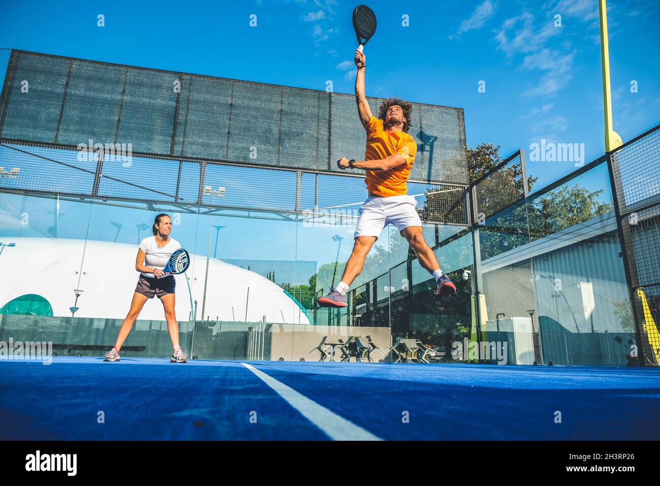 Gemischtes Padel-Match auf einem Padel-Platz mit blauem Gras - wunderschönes Mädchen und hübscher Mann, der im Freien Padel spielt Stockfoto