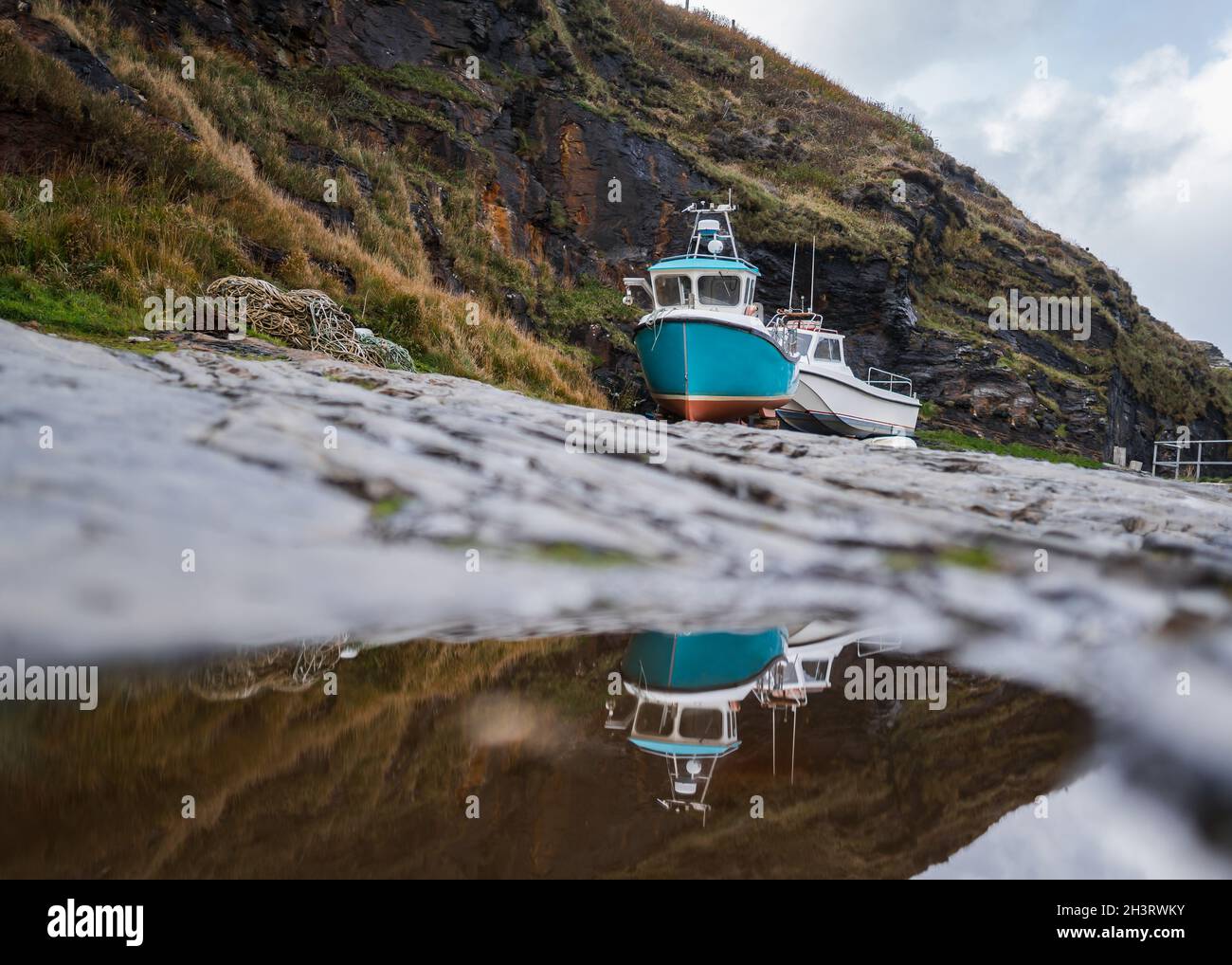 Alte Fischerboote in Trockendock Felswand Hafen vertäut schöne Landschaft im Wasser reflektiert. Wunderschöne Farben und dramatischer Himmel. Stockfoto