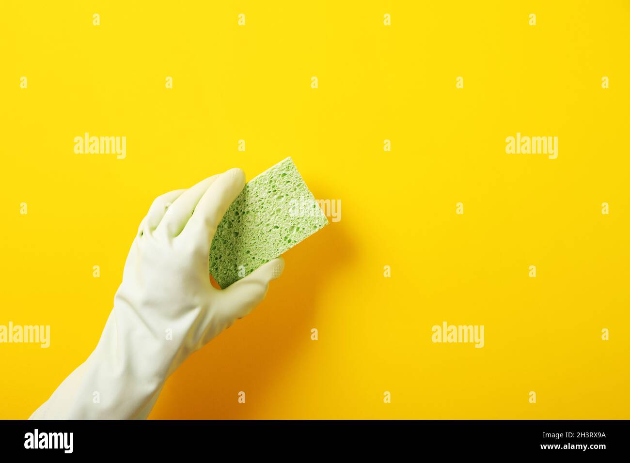 Eine Hand in einem grünen Gummihandschuh hält einen Waschschwamm über gelbem Hintergrund Stockfoto