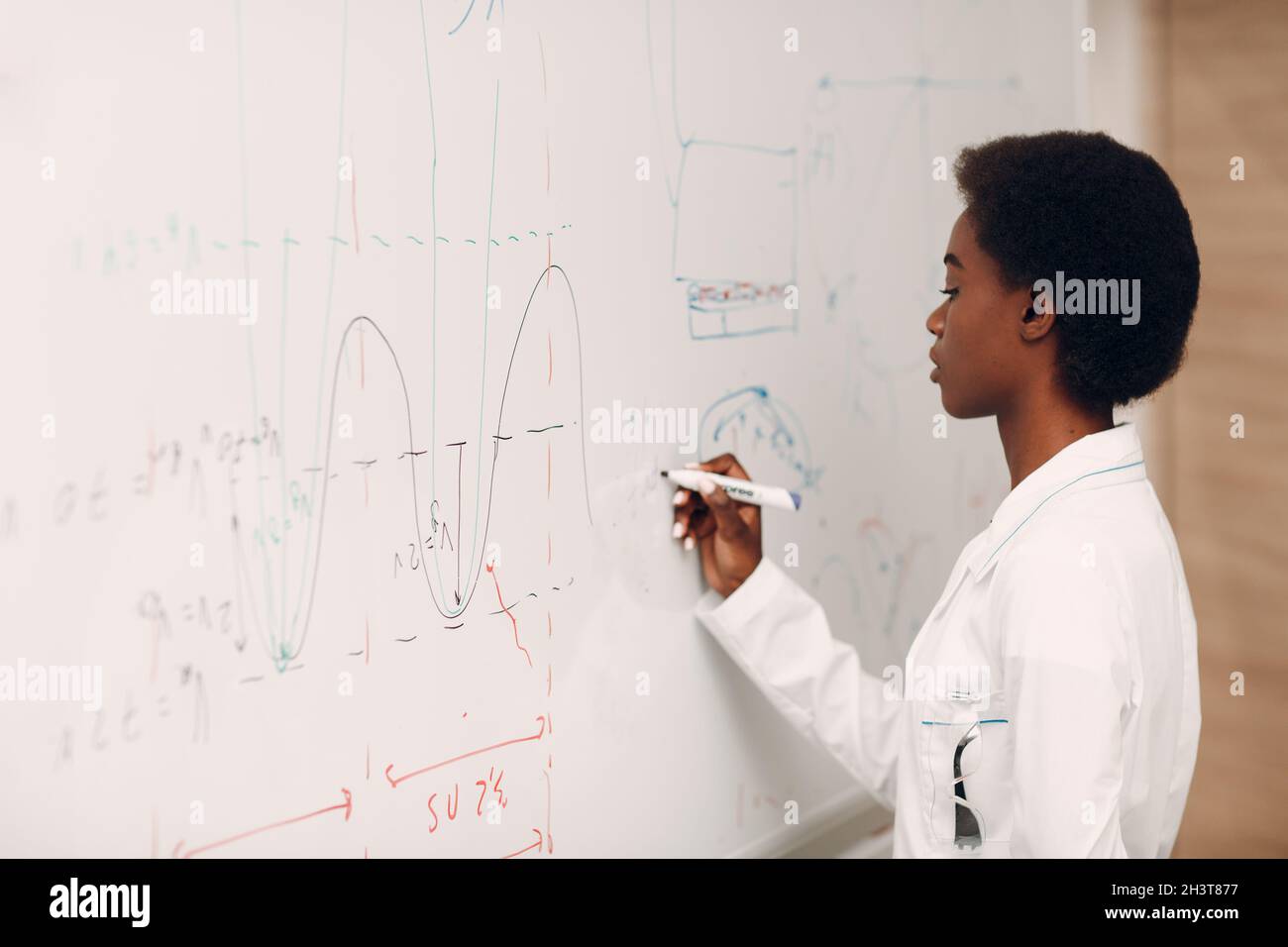 Afroamerikanische Mathematiklehrerin steht an der Tafel mit Marker Stockfoto
