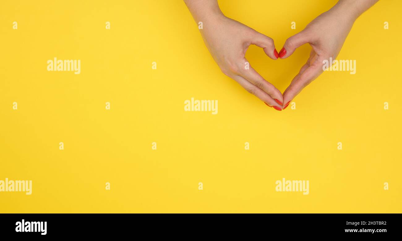 Zwei weibliche Hände gefaltet in Form eines Herzens auf einem gelben Hintergrund. Dankbarkeit und Freundlichkeit Konzept, Banner Stockfoto