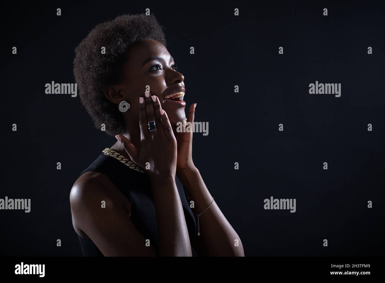 Beeindruckte junge afroamerikanische Frau mit erstaunlichem und glücklich bewundertem Ausdruck, isoliert auf schwarzem Hintergrund Stockfoto
