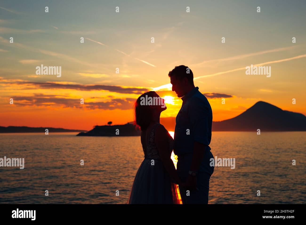 Die Braut und der Bräutigam stehen am Strand der Insel Mamula und halten sich beim Sonnenuntergang die Hände Stockfoto
