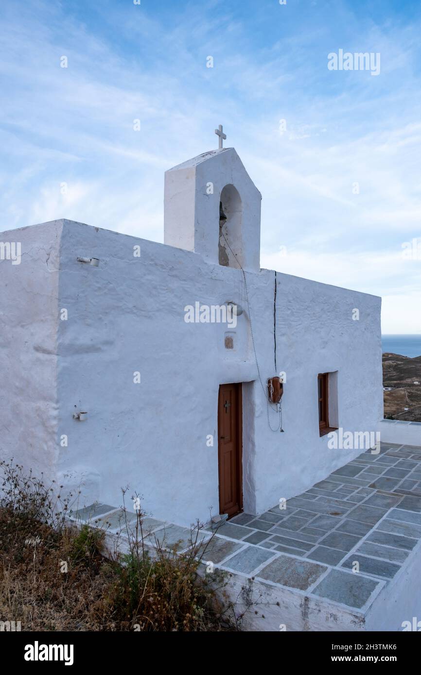 Serifos Island, Griechenland. Kleine alte Kapelle, weiße Wände und Glockenturm, griechisch-orthodoxe Kirche auf dem Hügel, wolkiger blauer Himmel im Hintergrund. Stockfoto