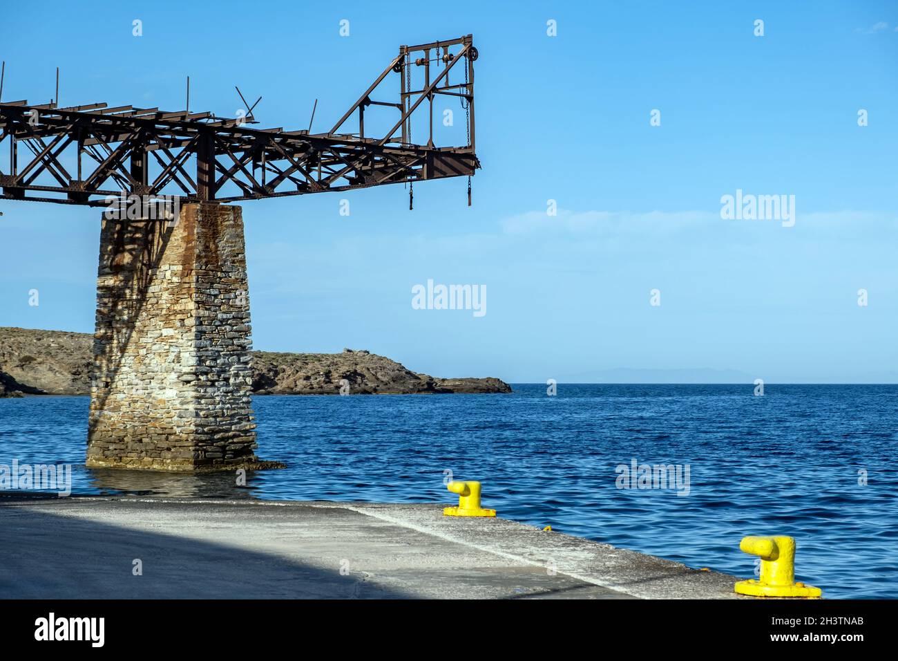 Alte rostige Eiseneisenbahn-Brücke auf Steinsockel und gelben Pollern am Hafen von Loutra Kythnos Kykladen Sommerziel Griechenland. Land, Stockfoto